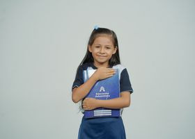 A young girl smiles while holding her school notebook, representing joy in education.