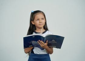 Young schoolgirl with long hair holding a book and pencil, deep in thought against a plain background.